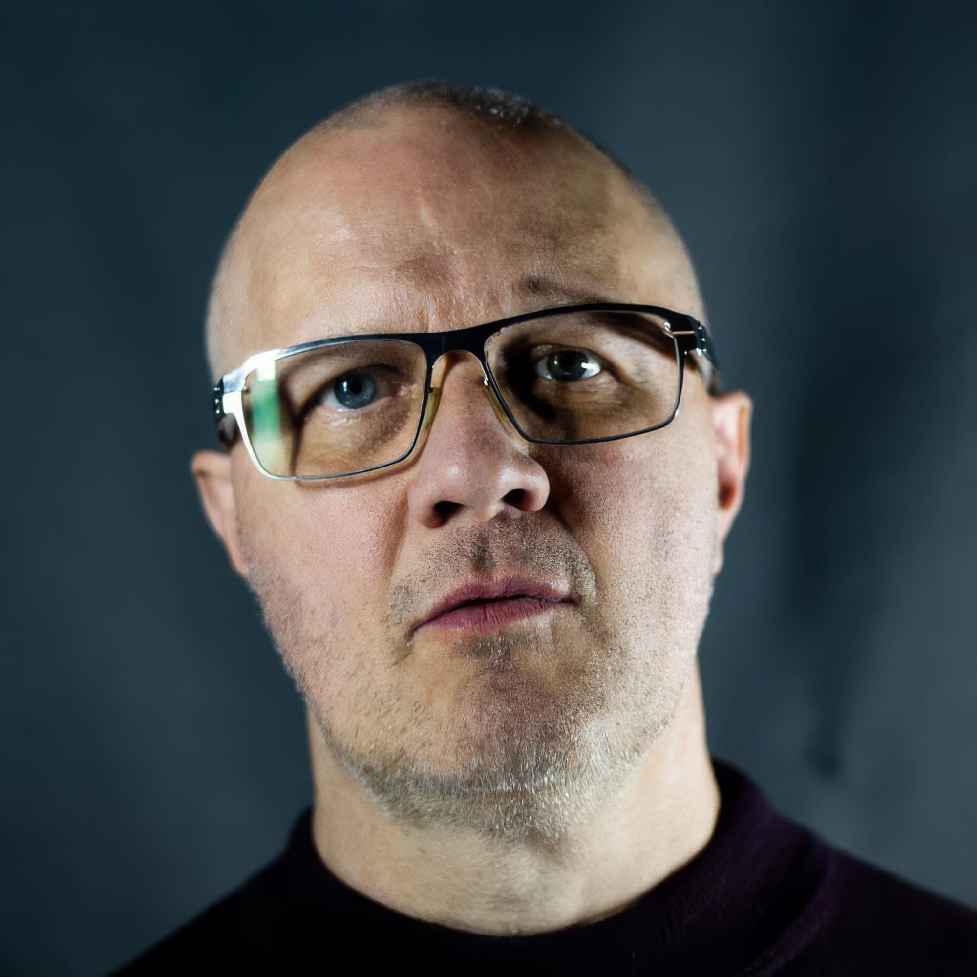 Candid photo of Jon wearing dark colours in front of a dark blue-grey background